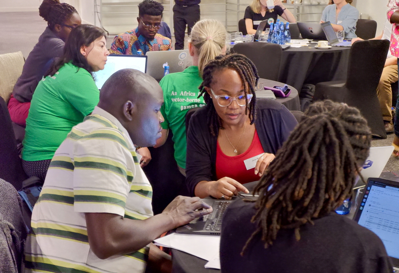 Students at the hackathon discussing genomic data at tables with laptops